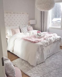 a white bed sitting in a bedroom next to a window covered in pink and white blankets