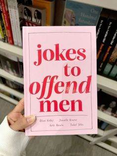 a person holding up a pink book in front of a bookshelf