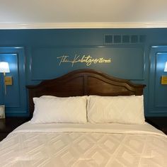 a bed with white sheets and pillows in a room that has blue walls, wooden headboard, and two lamps on either side