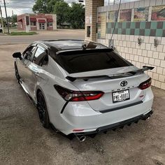 the rear end of a white car parked in front of a building with graffiti on it