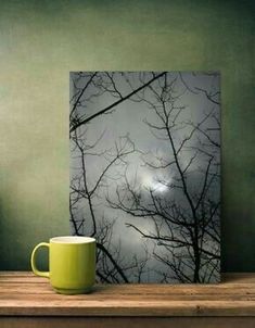 a green coffee mug sitting on top of a wooden table next to a framed photograph