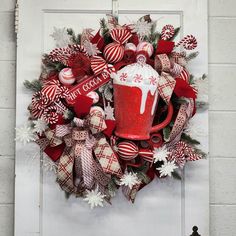 a christmas wreath with a mug and candy canes hanging on the front door,