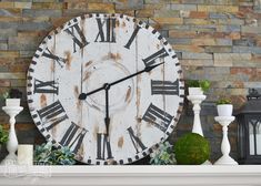 a large white clock sitting on top of a mantle next to flowers and vases