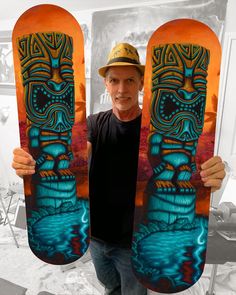 a man holding up two skateboards with an image of a tiki on it