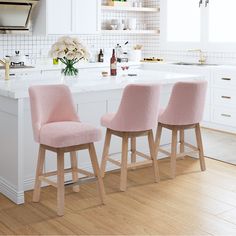 three pink chairs sitting in front of a white kitchen island with flowers on the counter