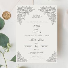 an elegant wedding card with flowers and leaves on the front is displayed next to some greenery