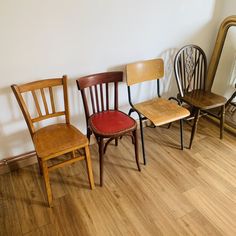 four wooden chairs lined up against a white wall in front of a mirror on the floor