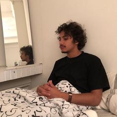 a young man sitting in bed looking at himself in the mirror and holding his hands together