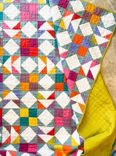 a colorful quilt sitting on top of a wooden table next to a yellow chair and blanket