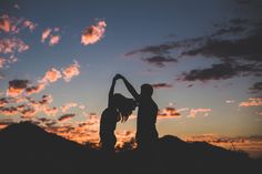 two people standing in the sunset with their arms around each other and one person holding his hand up