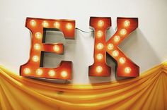 the letters e k are lit up in bright orange light bulbs and draping