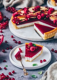 two slices of cheesecake with cranberry sauce on plates next to pomegranates