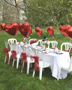 a table set up with red heart balloons and white chairs for a valentine's day party