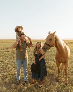 a man, woman and child are standing in the grass with a horse behind them