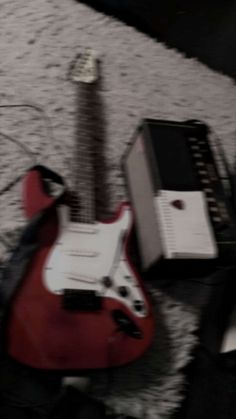 a red electric guitar sitting on top of a floor next to a speaker and amp