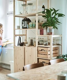 a woman standing in front of a wooden shelf filled with pots and pans next to a window