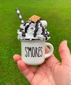 a hand holding a coffee cup filled with ice cream and toppings that says smores