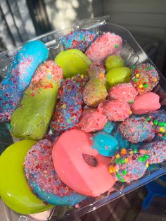 a plastic container filled with lots of different colored doughnuts and sprinkles