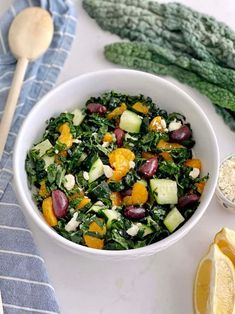 a white bowl filled with salad next to lemons and other vegetables on a table