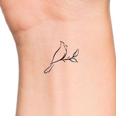 a small bird tattoo on the wrist is shown in black ink, and has a thin branch