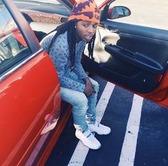 a young man sitting in the back of a red car with his hand on his hip