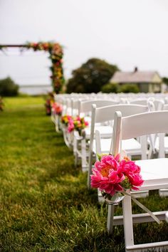 rows of white folding chairs with pink flowers on the back and seat, set up for an outdoor ceremony