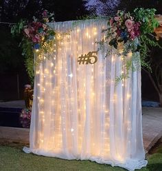 an outdoor wedding ceremony with lights and flowers on the back wall, decorated with sheer curtains