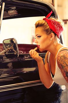 a woman leaning on the door of a black car with a red bow in her hair