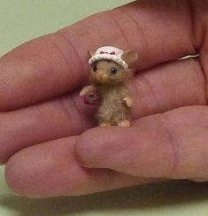 a tiny toy mouse is sitting in someone's hand, wearing a white hat