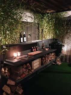 an outdoor bar is lit up with candles and bottles on top of firewood logs