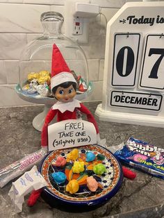 an elf is sitting next to a plate of candy and a sign that says, free take one simply use