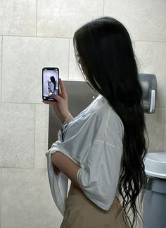 a woman standing in front of a toilet taking a selfie with her cell phone