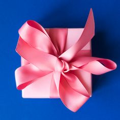 a pink gift box with a large bow on it's side against a blue background