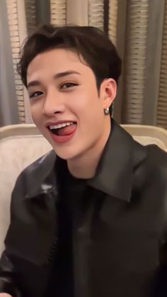 the young man is smiling while sitting in front of his laptop computer and wearing earrings