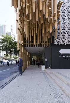 people are walking down the sidewalk in front of a building with wooden slats on it