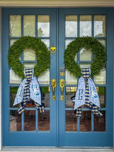 two wreaths are on the front doors of a house with blue and yellow ribbons