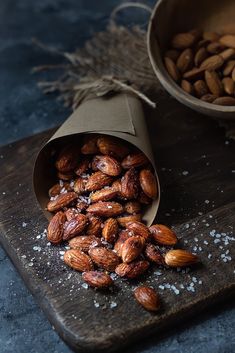 almonds in a paper bag on a cutting board next to a bowl of nuts