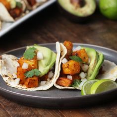 three tacos with avocado and cilantro are on a black plate