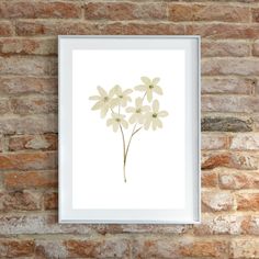 a white frame hanging on a brick wall next to a painting with flowers in it