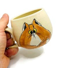 a hand holding a cup with a drawing of a cat on it