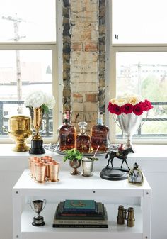 a white table topped with bottles and vases filled with flowers next to a window