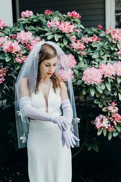 a woman in a white dress wearing gloves and a veil with pink flowers behind her