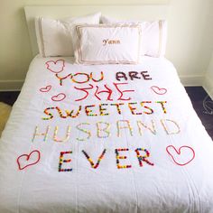 a bed with a white comforter covered in lots of colorful beads and words on it