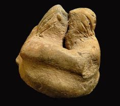 a stone sculpture of two people hugging each other with their hands together, against a black background