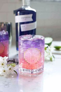 two glasses filled with purple and pink liquid sitting on top of a counter next to a bottle