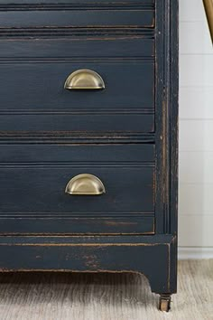 an old black dresser with brass handles and knobs on the bottom drawer, next to a chair