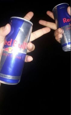 two people hold up red bull energy drink cans in their hands, with the word red bull written on them