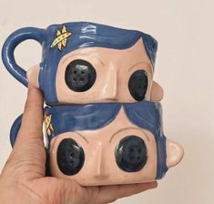 two coffee mugs with faces on them being held up