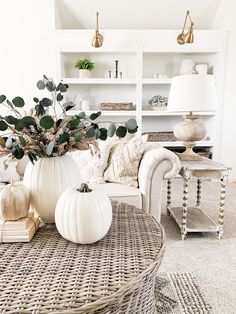 a living room with white pumpkins and greenery in the centerpiece on top of a wicker coffee table