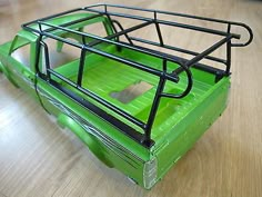 a green toy truck with a cage on the top and bottom rack, sitting on a wooden floor